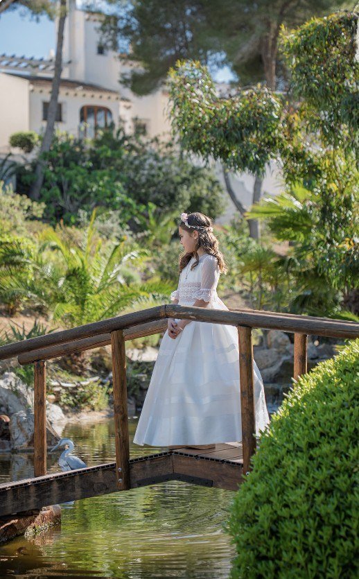 Niña de comunión en un puente de madera de un jardín